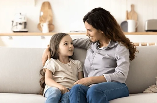 Parent talking calmly with a young child at eye level on a couch