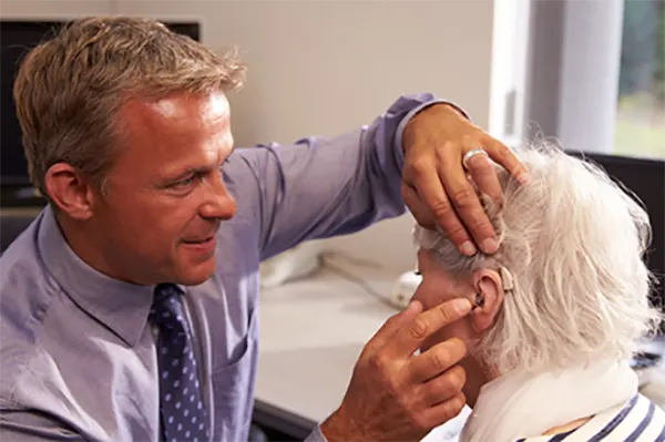 Older adult being fitted with a modern hearing aid by an audiologist