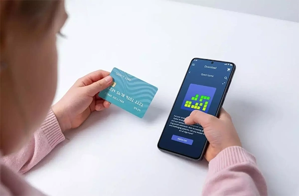 A parent looking at a bank statement on a phone beside a games console controller.